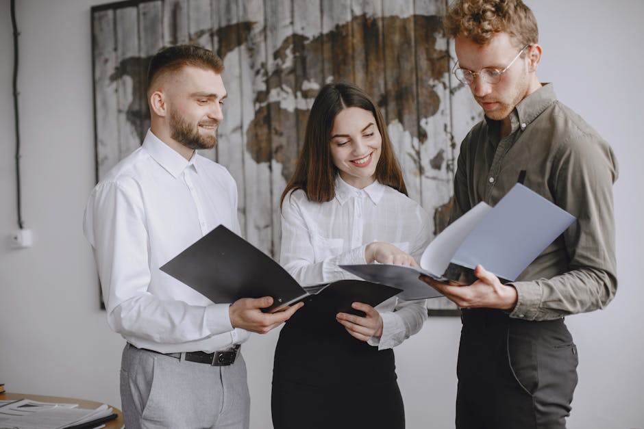 Three young professionals collaborating in an office, reviewing documents together with smiles and focus.
